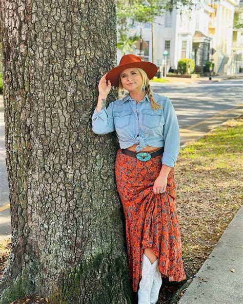 A Woman Leaning Against A Tree Wearing A Cowboy Hat And Dressy Skirt