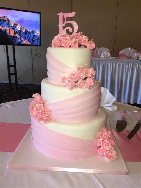 a three tiered cake with pink flowers on the table and a tv in the background