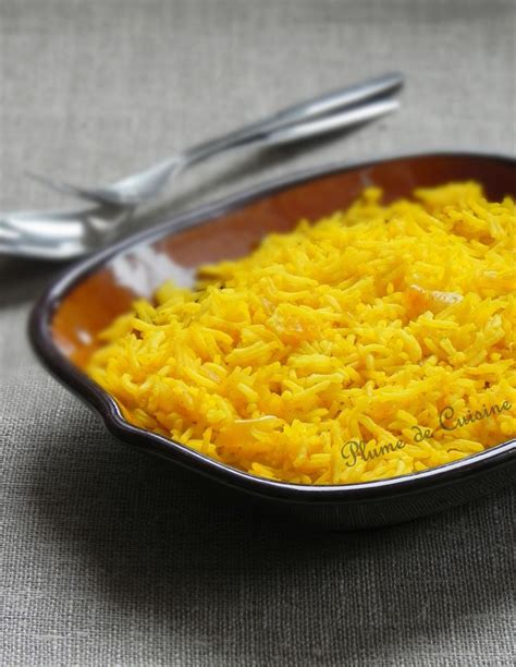 A Bowl Filled With Yellow Rice On Top Of A Table Next To Two Silver Spoons