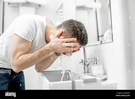 Man Washing His Face With Fresh Water And Foam In The Sink At The White