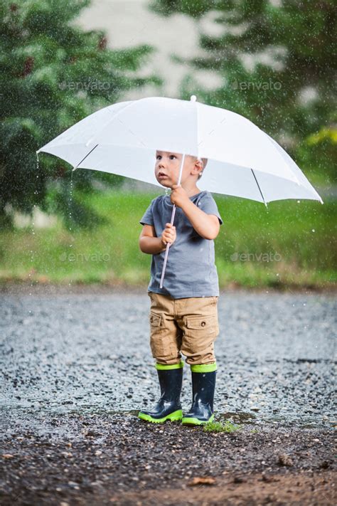 Adorable Child Holding An Umbrella In A Rain Storm Stock Photo By