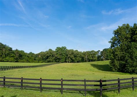 A Rollling Green Field Surrounded By Trees And A Wooden Fence In A