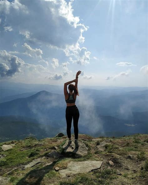 A Woman Standing On Top Of A Mountain With Her Arms Up In The Air While