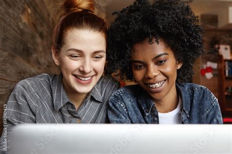 Two Happy Lesbians Sitting In Front Of Open Laptop Computer Together Looking At Screen With