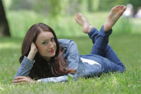 A Woman Laying In The Grass With Her Feet Up And Arms Behind Her Head Looking At The Camera