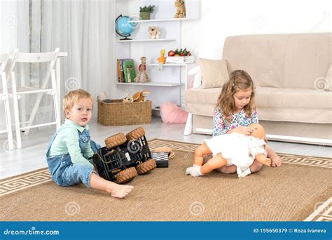 Little Children Sit On The Floor On A Rug In The Room At Home And Play