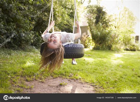 Portrait Of Young Girl Playing On Tire Swing In Garden Stock Photo By