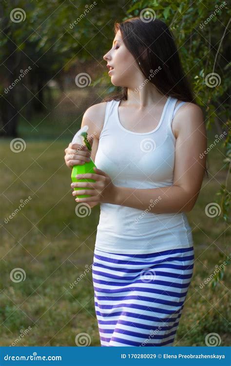 Young Woman Spraying Water On Herself From A Spray Bottle In A Summer