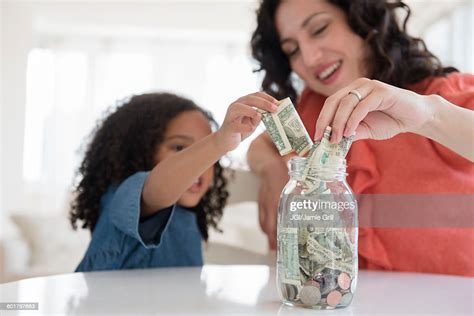 Mother And Daughter Saving Money In Jar Photo Getty Images