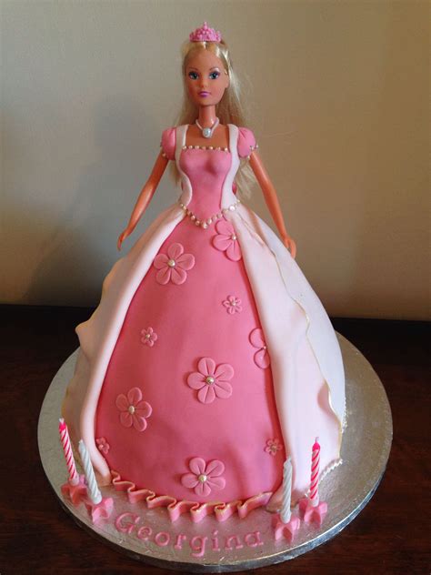 A Barbie Doll Cake With Pink And White Frosting On Its Side Sitting