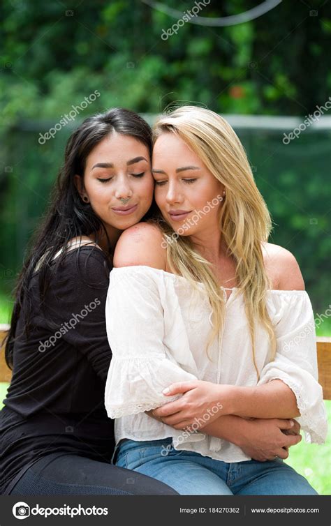 A Pair Of Proud Lesbian In Outdoors Brunette Woman Is Hugging A Blonde Woman In A Garden