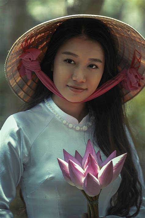 A Woman In A Conical Hat And Silk Clothing Holds A Flower In Can Tho
