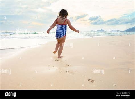 Little Girl In Bikini Running On The Idyllic Sandy Beach Near The Coast