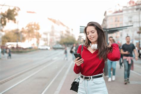 selective focus photo of woman in red sweater and blue denim jeans using her phone while