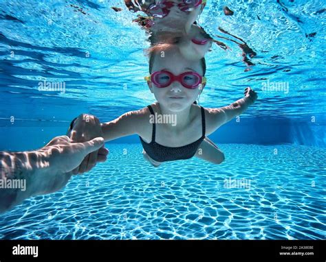 Girl Swimming Underwater In A Swimming Pool With The Help Of Her Father