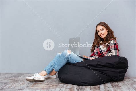 Cheerful Attractive Young Woman Sitting And Using Laptop On Black Bean