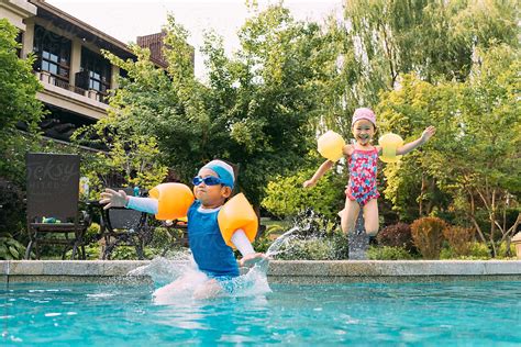 Two Kids Jumping Into Swimming Pool Del Colaborador De Stocksy