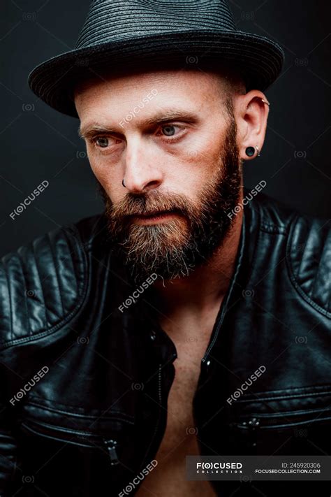 Cool Hipster In Hat And Leather Jacket Looking Away On Black Background — Thoughtful Caucasian