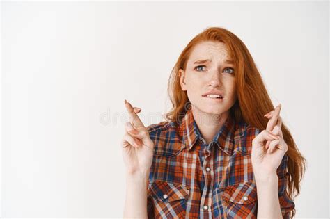 worried redhead girl biting lip and looking up with hope cross fingers while making a wish or