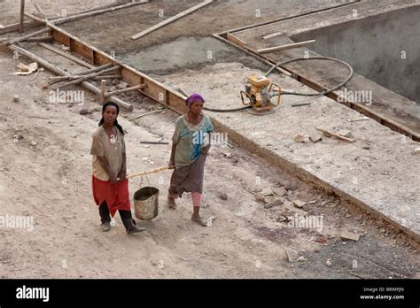 Two Female Construction Workers Carrying Wet Cement In A Bucket Carried