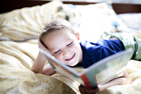 Boy Laughing While Reading A Book On A Bedt20grzpym