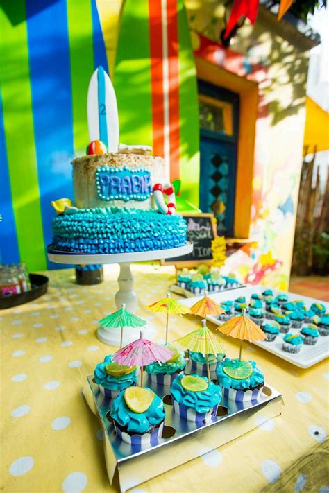 A Table Topped With Cupcakes Covered In Blue Frosting Next To A Cake
