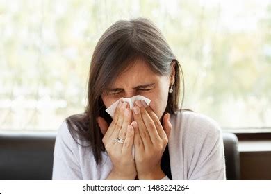 Brunette Woman Blowing Nose Into Tissue Stock Photo