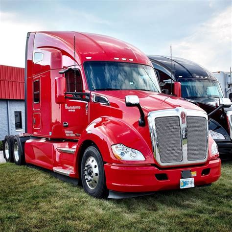 A Red Semi Truck Parked Next To Other Semi Trucks In A Grassy Area Near