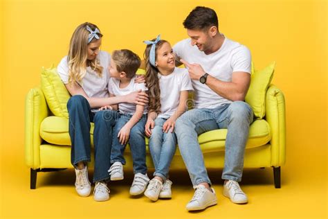 Parents Talking With Kids While Sitting Together On Sofa On Yellow