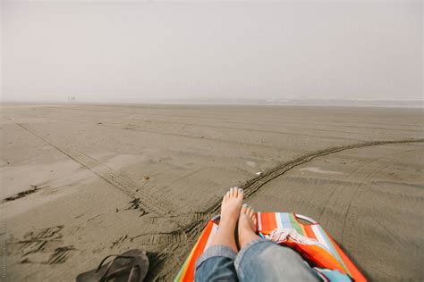 Woman Relaxes Barefoot In Lounge Chair On Beach On Misty Morning Del Colaborador De Stocksy