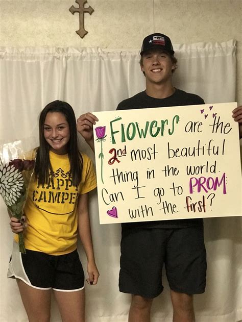 Two People Standing Next To Each Other Holding Flowers And A Sign That