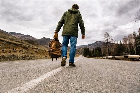 Man With Backpack In Hand Walking Alone Down A Mountain Road Stock Photo E Serebryakova