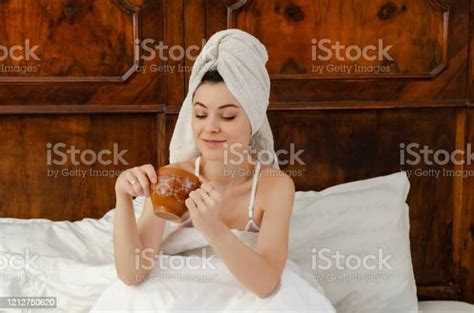 Woman Sitting In Bed After Shower With A Towel On Her Head And A Stock
