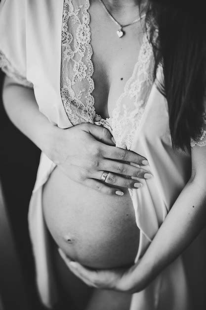 Беременная женщина держится за руки вокруг живота девушка обнимает круглый живот у окна дома