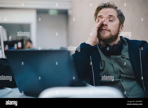 Tired Computer Programmer Rubbing Eyes While Sitting In Office Stock