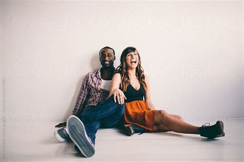 Cute Young Interracial Couple Laughing Sitting On Apartment Floor By