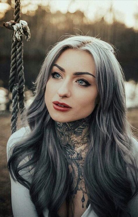 A Woman With Grey Hair And Tattoos On Her Chest Sitting In Front Of A Rope