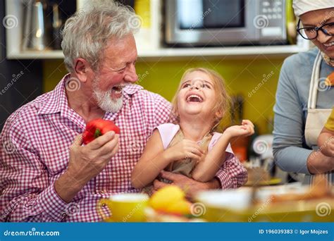 Granddaughter Sitting In The Lap Of A Grandpa In The Kitchen Laughing Together Royalty Free