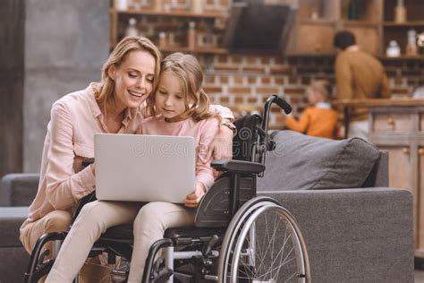 Smiling Mother And Little Daughter In Wheelchair Using Laptop Together