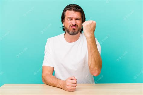 premium photo middle age dutch man sitting isolated on blue background showing fist to camera