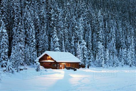 A Snow Covered Log Cabin On A Snow Covered Lakeshore Surrounded By