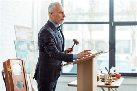 Side View Of Auctioneer Holding Wooden Gavel And Looking Away During