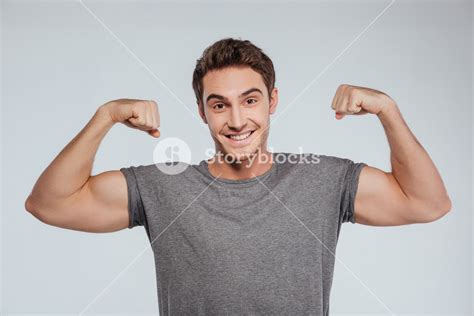 Portrait Of A Smiling Srtong Man Flexing Biceps Isolated On The Gray