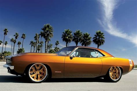 An Orange Muscle Car With Gold Rims Parked In A Parking Lot Next To