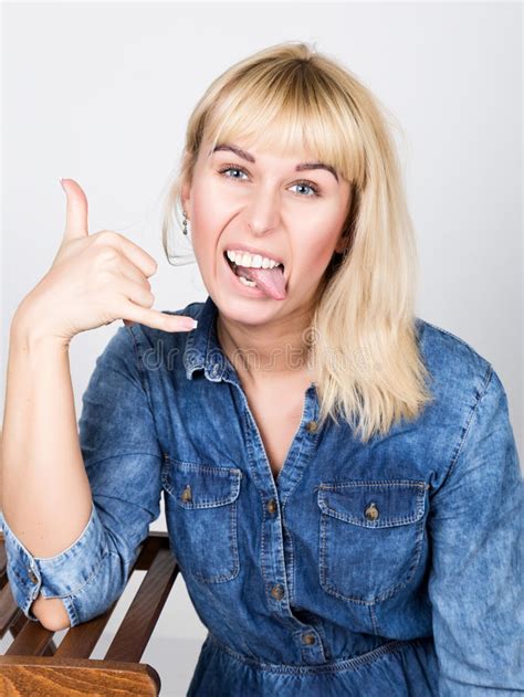 beautiful blonde girl wearing a denim shirt showing tongue and fingers makes shaka sign stock