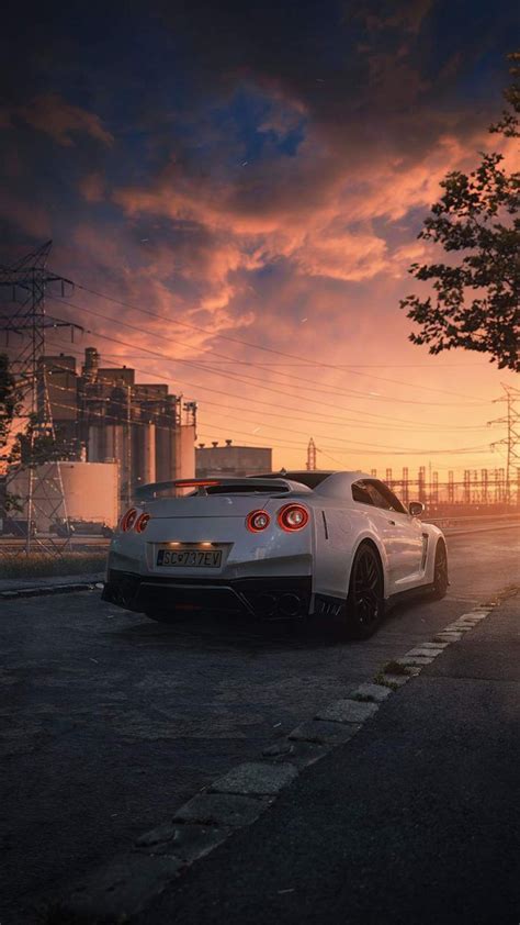 A White Sports Car Parked In Front Of An Industrial Building At Sunset