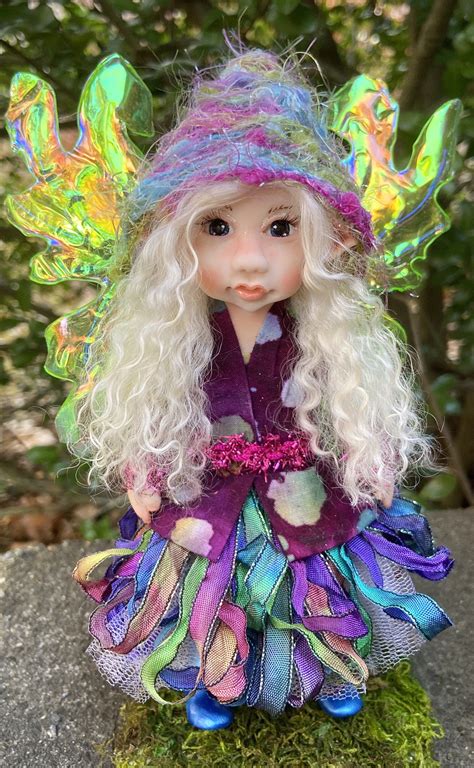 A Doll With Long White Hair Wearing A Purple Dress And Green Hat