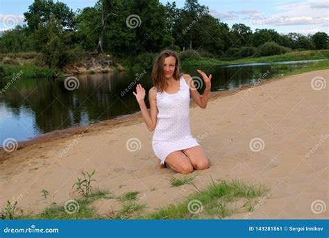 Girl Sitting On Her Knees In The Sand On The River Bank Stock Image
