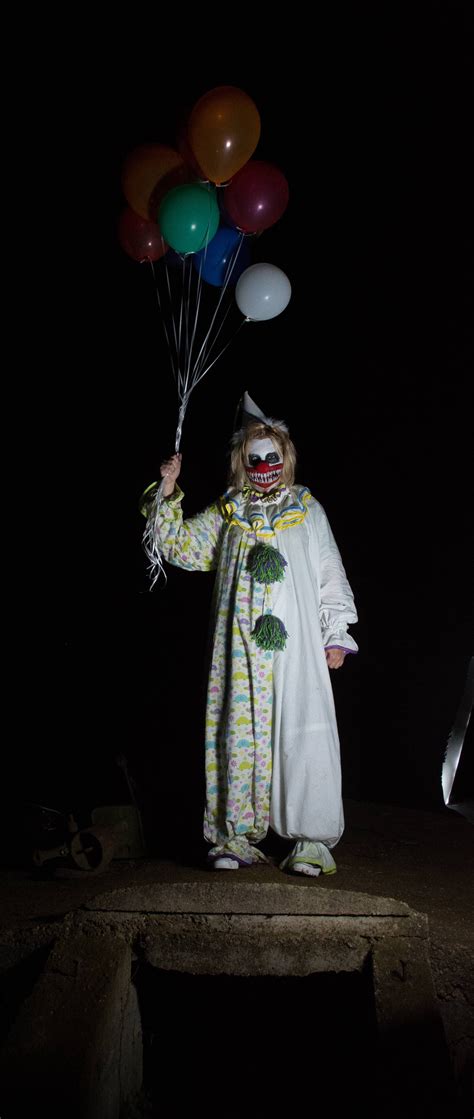 A Scary Clown Holding Balloons In The Dark