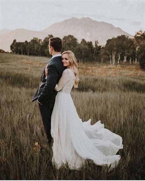 A Bride And Groom Standing In The Middle Of A Field With Mountains In